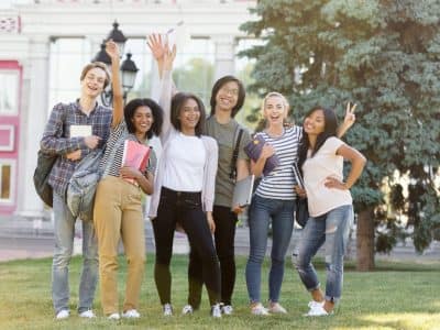 Image of multiethnic group of young cheerful students standing and waving outdoors. Looking at camera.